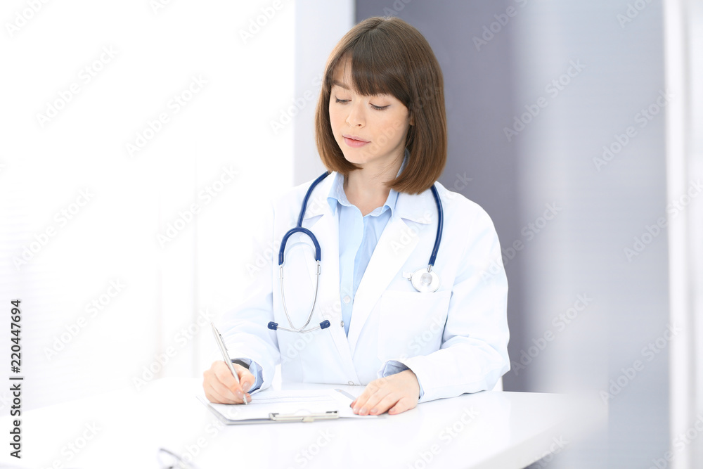 Doctor woman at work. Female physician filling up medical form while sitting the table in clinic or hospital. Medicine and healthcare concept for advertising Doctor woman at work. Female physician filling up medical form while sitting the table in clinic or hospital. Medicine and healthcare concept for advertising