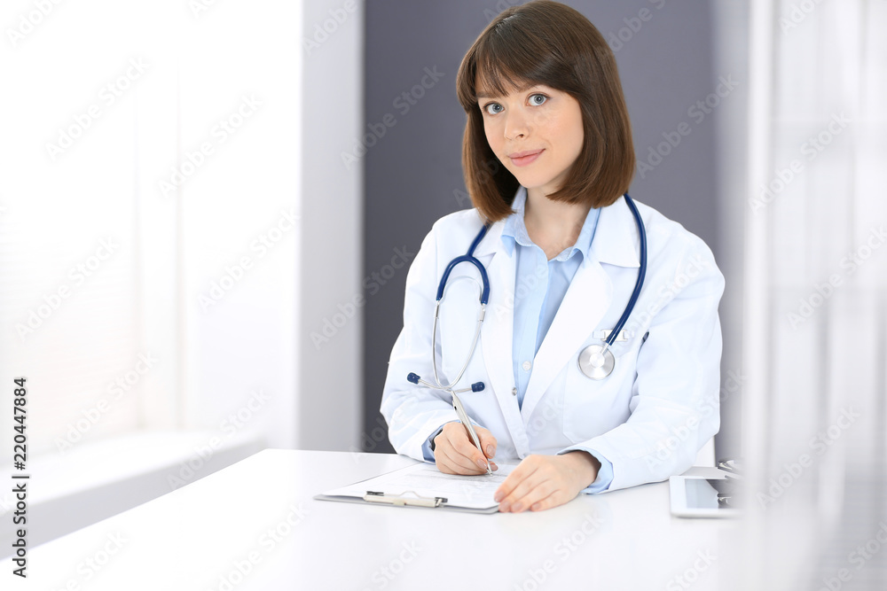 Doctor woman at work. Female physician filling up medical form while sitting the table in clinic or hospital. Medicine and healthcare concept for advertising Doctor woman at work. Female physician filling up medical form while sitting the table in clinic or hospital. Medicine and healthcare concept for advertising