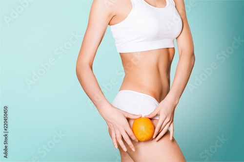 Female slender body in sport underwear holding orange on