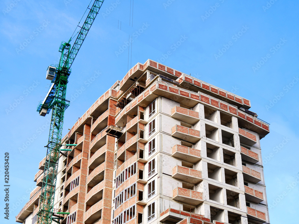 Hoisting crane near building under construction. Building site.