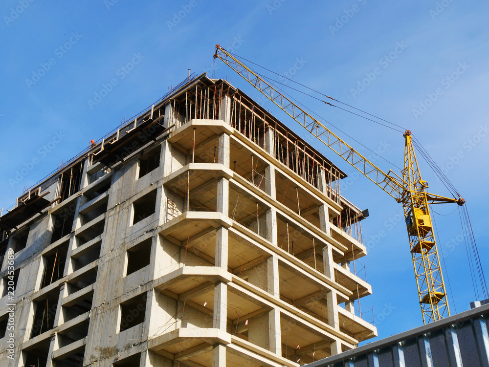 Construction crane and concrete building under construction against blue sky. Construction site.