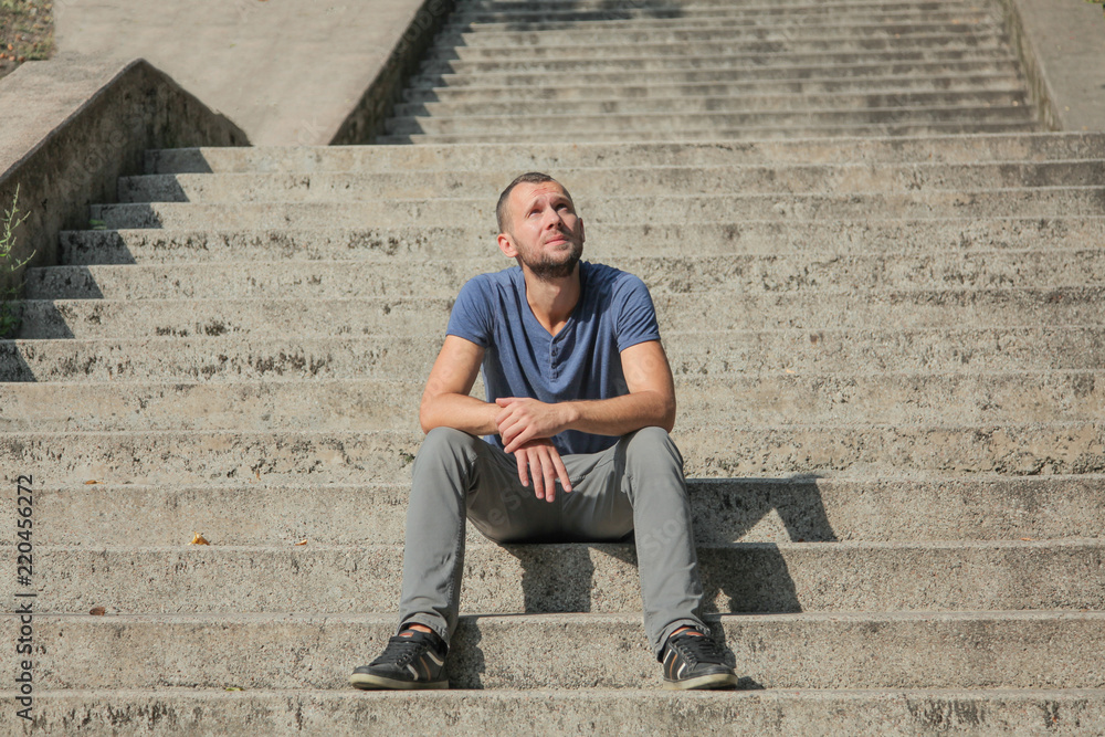 the man is sitting on the steps of the staircase in a relaxed pose on a sunny afternoon the man is sitting on the steps of the staircase in a relaxed pose on a sunny afternoon