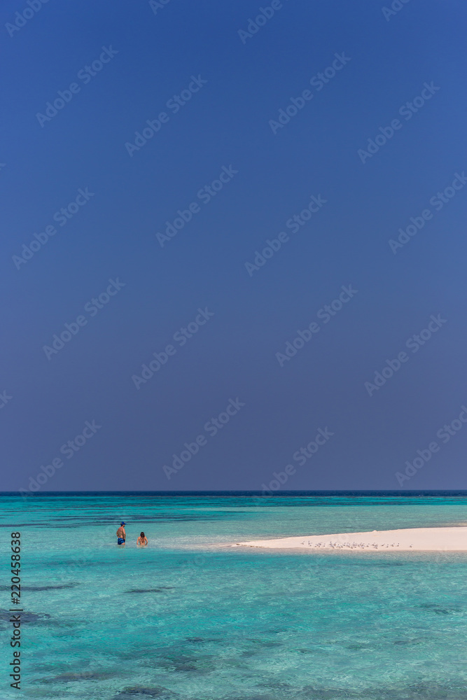Maldives, Feb 8th 2018 - Tourists swimming in a turquoise blue sea, desert island, small traditional hut hotel on a blue sky day, paradise feeling in Maldives.