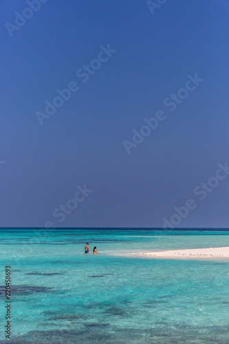 Maldives, Feb 8th 2018 - Tourists swimming in a turquoise blue sea, desert island, small traditional hut hotel on a blue sky day, paradise feeling in Maldives.