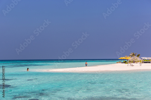 Maldives, Feb 8th 2018 - Tourists swimming in a turquoise blue sea, desert island, small traditional hut hotel on a blue sky day, paradise feeling in Maldives. © LMspencer