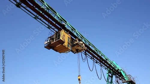 Construction crane with cargo winch, hoist rope and hook against clear blue sky. Lifting mechanism of equipment with control cabin. photo