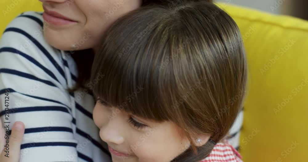 Close up of the Caucasian mother and small daughter sitting on the yellow couch and then hugging cheerfully. Close up of the Caucasian mother and small daughter sitting on the yellow couch and then hugging cheerfully.