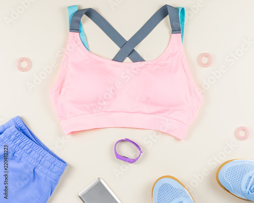 Woman sport clothes, sneakers, headphones and fitness tracker on neutral background. Sport fashion concept. Flat lay