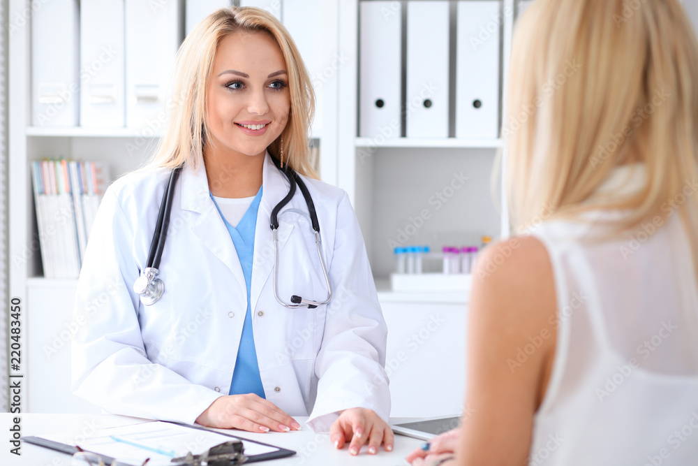 Doctor and patient discussing something while sitting at the table at hospital. Medicine and health care concept Doctor and patient discussing something while sitting at the table at hospital. Medicine and health care concept