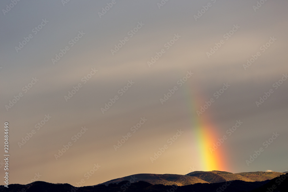 Beautiful and surreal view of part of a rainbow over some hills