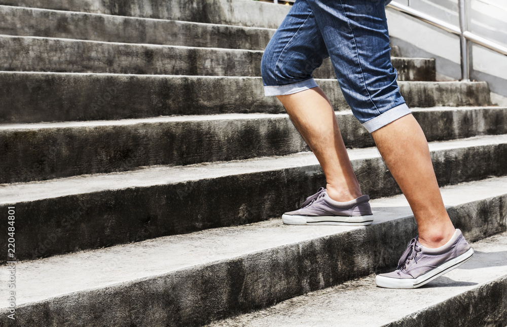 Young man in blue jeans and sneaker shoes walking up stairs outdoors background with copy space for text. Concept of person's lifestyle. Young man in blue jeans and sneaker shoes walking up stairs outdoors background with copy space for text. Concept of person's lifestyle.
