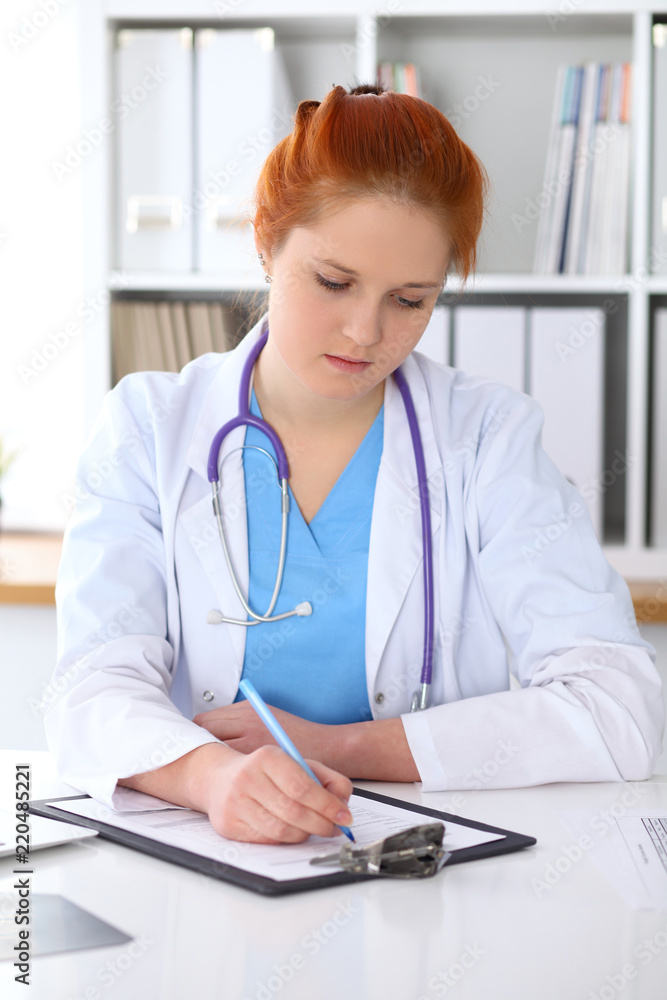Ginger female doctor filling up medical form on clipboard closeup. Healthcare, insurance and medicine concept Ginger female doctor filling up medical form on clipboard closeup. Healthcare, insurance and medicine concept
