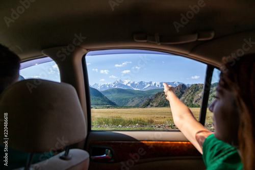 Close-up of a young tourist showing his finger the direction of traffic for a further adventure on top of a mountain in car covered with snow against a blue sky background.