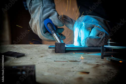 Tableau sur toile Strong man welder in work clothes hard working and welds with a welding machine metal
