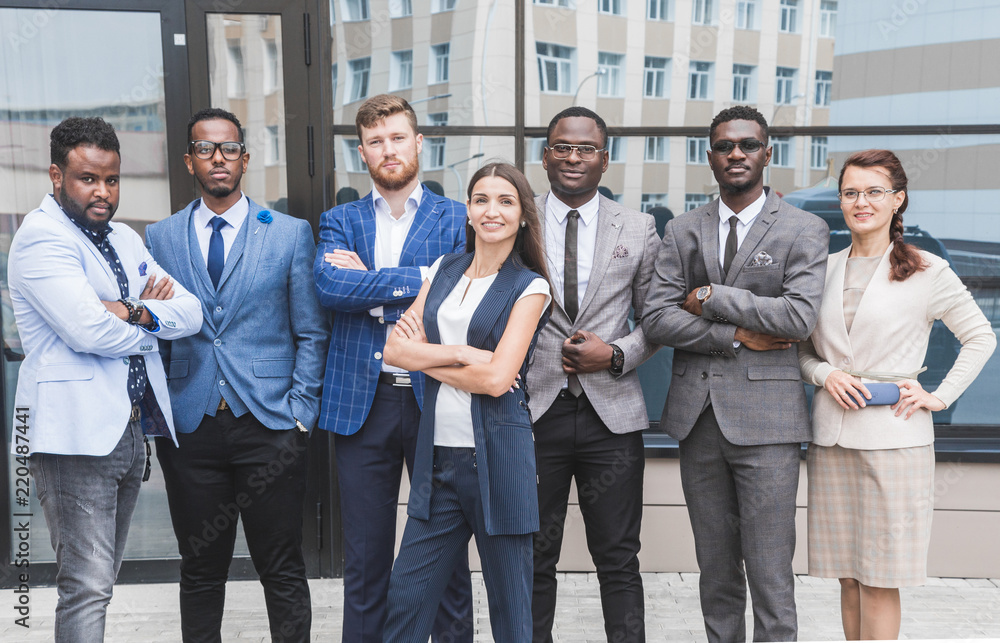 Successful company with happy workers. Men and women in business suits stand with their arms crossed against the background of skyscrapers Successful company with happy workers. Men and women in business suits stand with their arms crossed against the background of skyscrapers