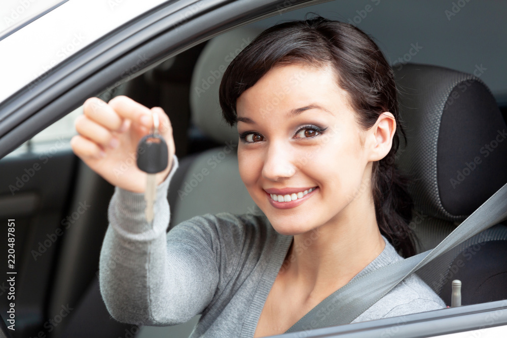 Happy owner of a new car is showing the car key. Pretty girl driver