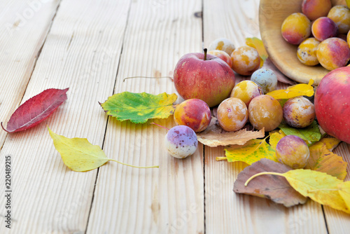 apples and mirabelles in autumnal leaves put on a wooden table