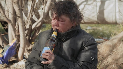 Portrait homeless woman vagabond in a temporary place is drinking beer. photo