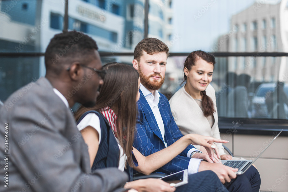 Obraz premium Group of happy diverse male and female business people team in formal gathered around laptop computer in bright office against the background of a glass building