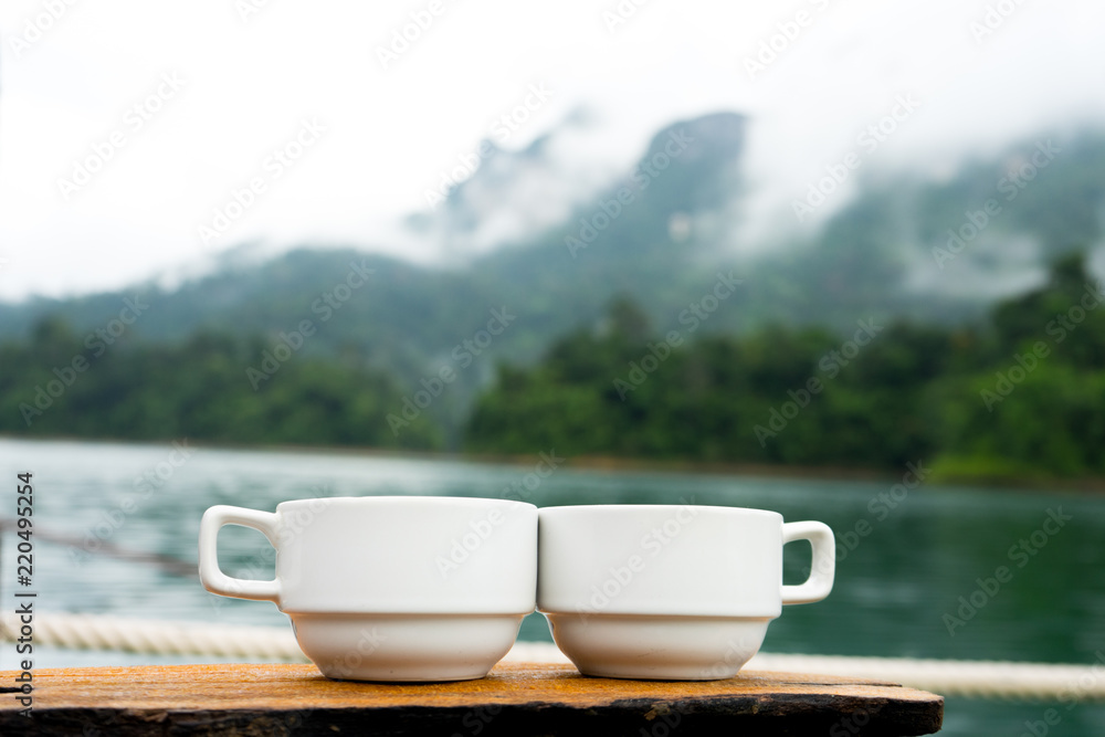 Couple or two coffee cups on the grass over lake with mountains landscape.  Beauty nature