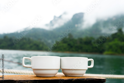 Couple or two coffee cups on the grass over lake with mountains landscape. Beauty nature