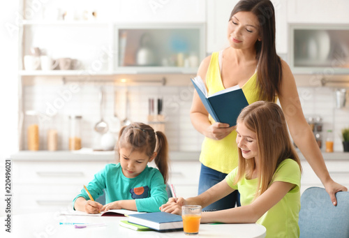 Cute little sisters doing homework with mother in kitchen