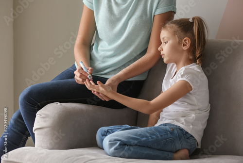 Billede på lærred Woman taking sample of her diabetic daughter's blood using lancet pen at home