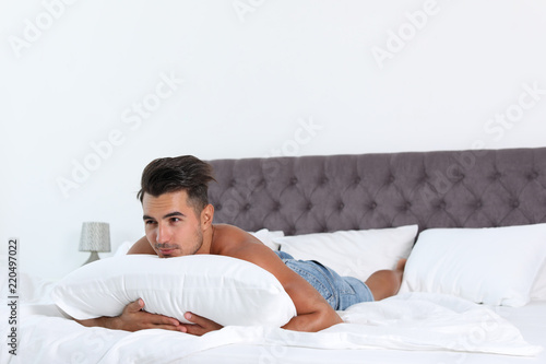 Sexy young man with soft pillow on bed at home