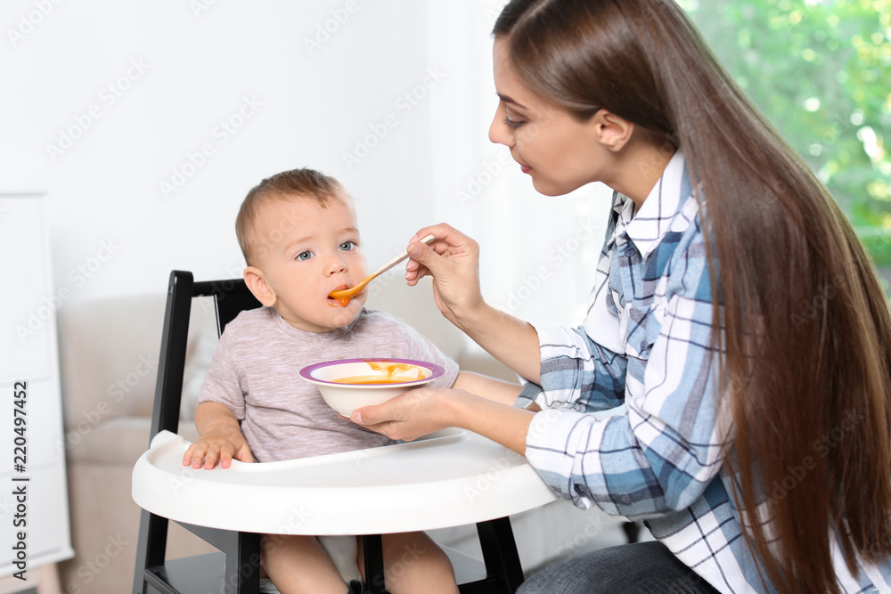 Woman feeding her child in highchair indoors. Healthy baby food Woman feeding her child in highchair indoors. Healthy baby food