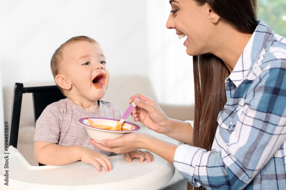 Woman feeding her child in highchair indoors. Healthy baby food Woman feeding her child in highchair indoors. Healthy baby food