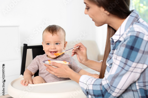 Woman feeding her child in highchair indoors. Healthy baby food