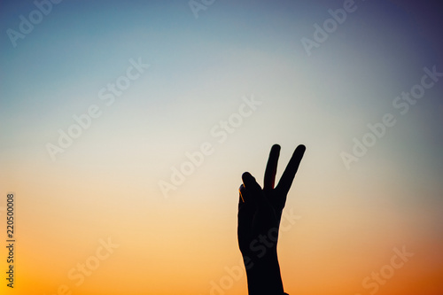 Female hand shows silhouette sign of victory or peace at sunset, copy space