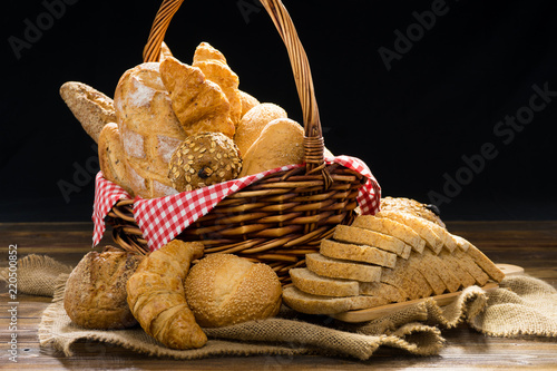 Various types of bread baking in wicker bread with red napkin on wooden table