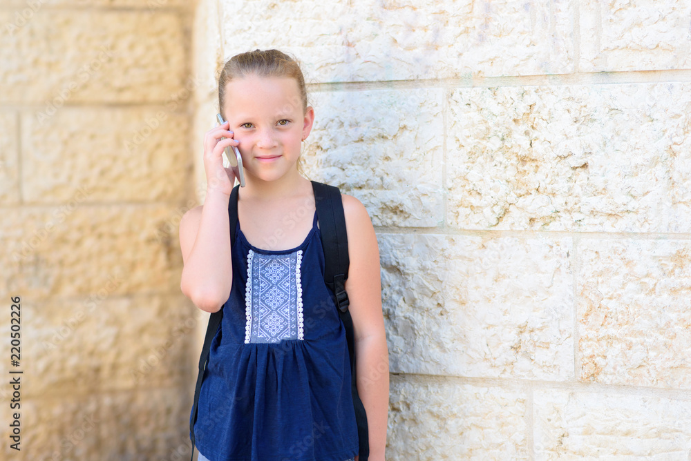 Outdoor portrait of happy girl 8-9 year old talking on phone. Cute schoolgirl with backpack talking on mobile phone and smiling. Outdoor portrait of happy girl 8-9 year old talking on phone. Cute schoolgirl with backpack talking on mobile phone and smiling.