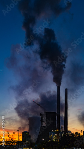 Cooling towers and chimneys of a petrochemical plant in the early morning. Dark sky with the red glowing of the morning sun at the horizon.