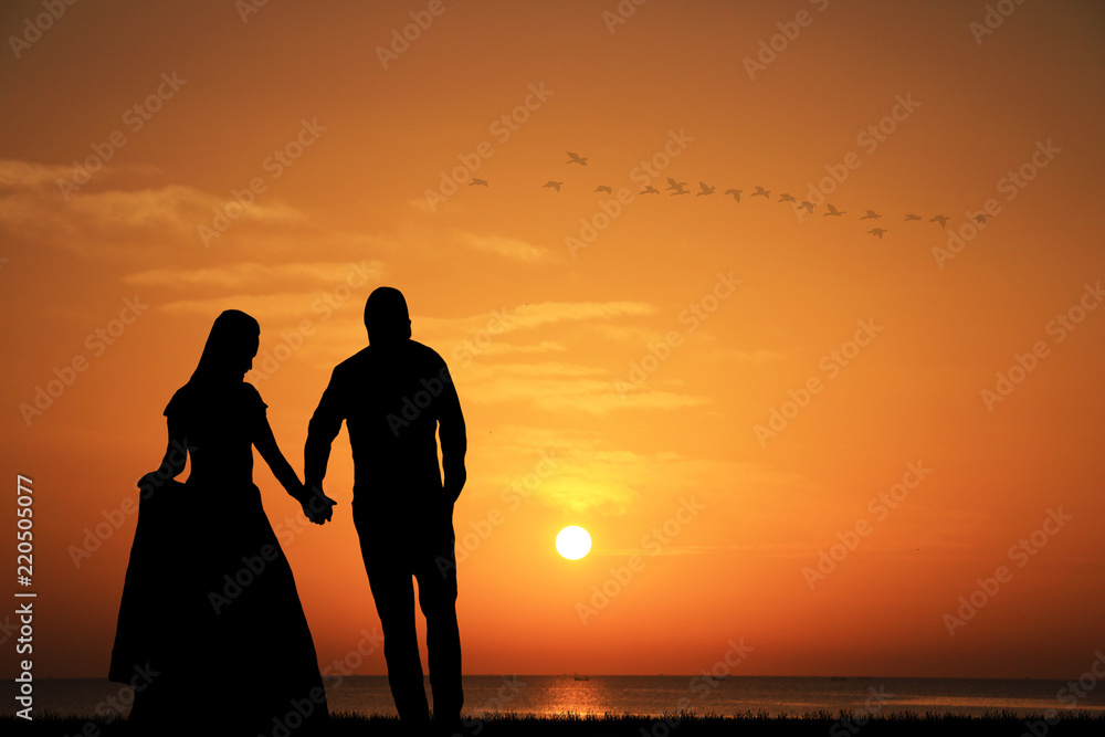 silhouette wedding couple is walking in the water on summer beach. Sunset over the sea