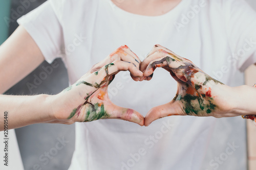 Closeup of woman's hands painted with watercolors in form of a heart, selective focus