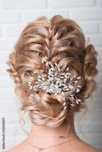 Wedding hairstyle on the head of a blonde close-up back view on a white brick wall background.
