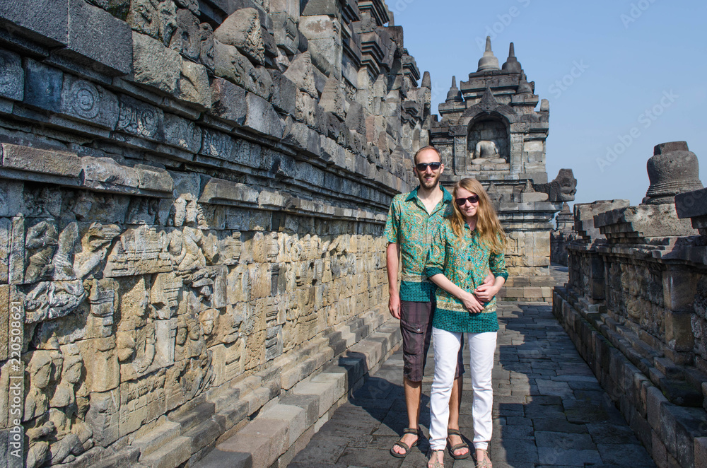 Young caucasian couple hugging in Borobudur temple in traditional indonesian batic shirts.