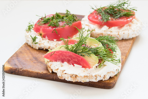 round crisp breads with cheese, tomatoes and avocado on a cutting board
