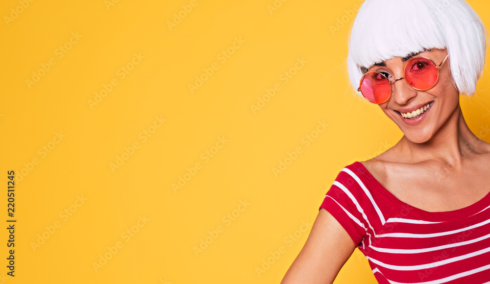 Beautiful young woman in blonde wig and pink sunglasses having fun on orange background, fashion blonde posing Beautiful young woman in blonde wig and pink sunglasses having fun on orange background, fashion blonde posing