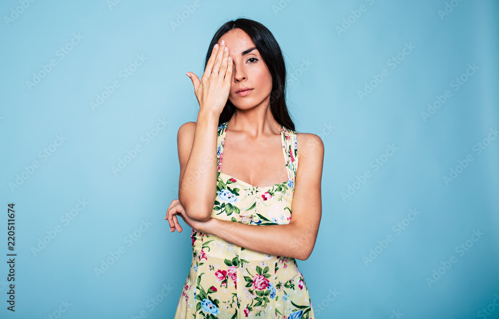 Young attractive brunette woman closed one eye with help of her hand on blue background Young attractive brunette woman closed one eye with help of her hand on blue background
