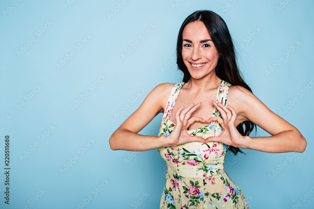 My heart is for you my love. Beautiful smiling brunette girl shows heart sign with help of hands isolated on blue background My heart is for you my love. Beautiful smiling brunette girl shows heart sign with help of hands isolated on blue background