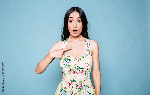 Young emotional and surprised woman pointing finger on herself isolated over blue background