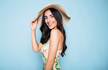 Portrait of cute summer brunette woman in hat and colorful dress, stylish girl have a fun and posing on blue background