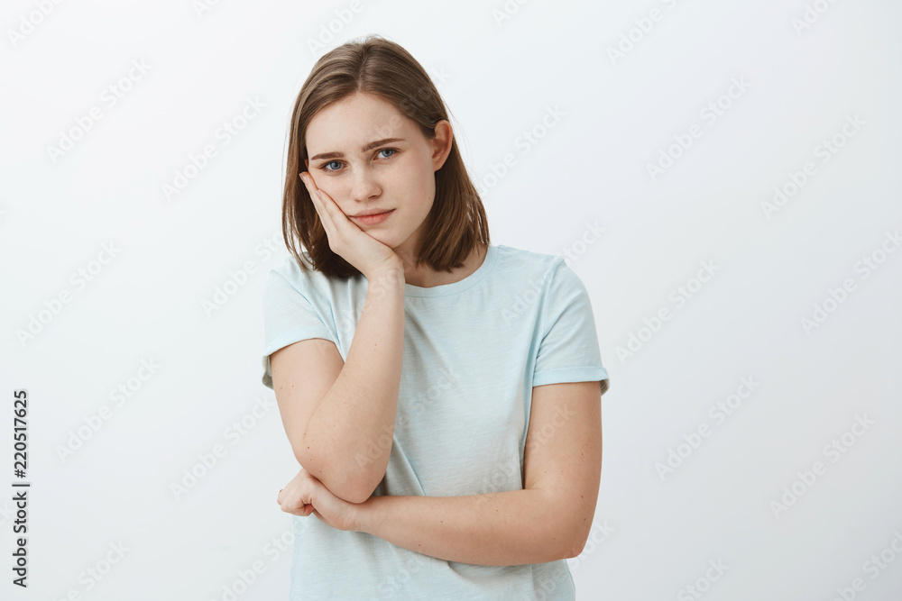 Girl feeling bored from routine. Portrait of calm good-looking european female leaning head on palm gazing at camera with tiresome and indifferent look having nothing to do standing against grey wall Girl feeling bored from routine. Portrait of calm good-looking european female leaning head on palm gazing at camera with tiresome and indifferent look having nothing to do standing against grey wall
