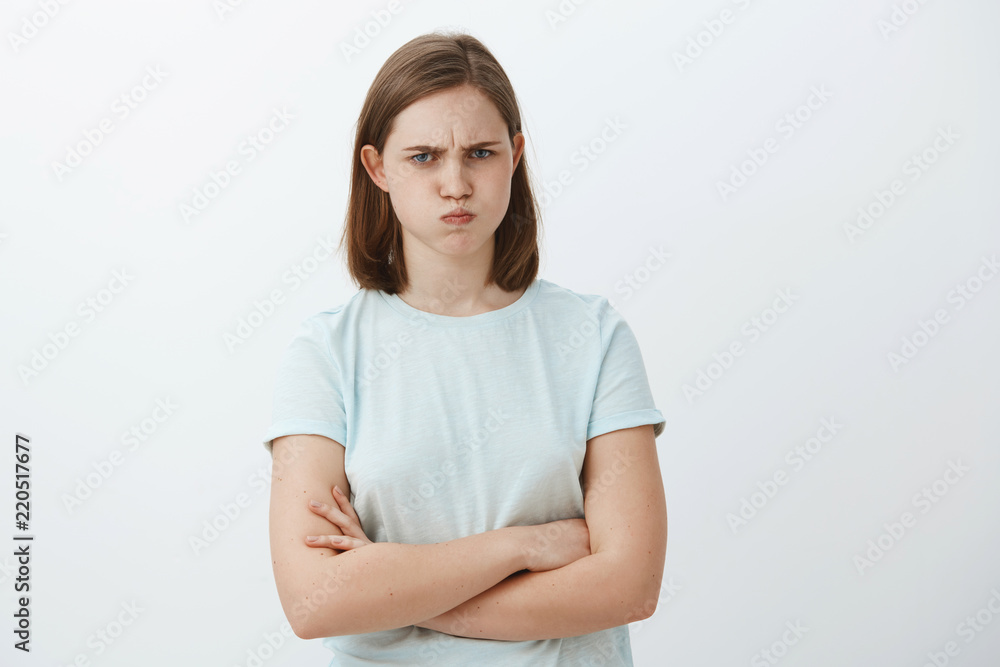 Studio shot of cute mad or offended female with flapped ear sulking and frowning crossing arms on chest standing in insulted pose being displeased or angry at someone over gray background Studio shot of cute mad or offended female with flapped ear sulking and frowning crossing arms on chest standing in insulted pose being displeased or angry at someone over gray background