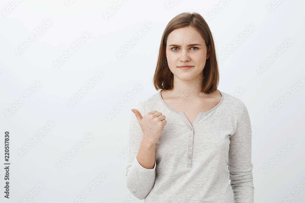 Girl unwilling bring lame classmate to party pointing backwards with thumb smirking displeased and dissatisfied rejection offer disapproving bad choice of friend standing unimpressed against grey wall Girl unwilling bring lame classmate to party pointing backwards with thumb smirking displeased and dissatisfied rejection offer disapproving bad choice of friend standing unimpressed against grey wall