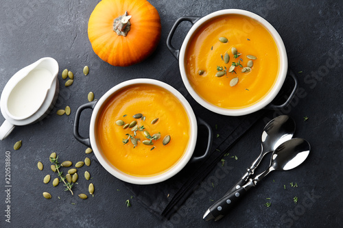 Pumpkin soup with thyme herb, cream and pumpkin seeds served in two black bowls, top view