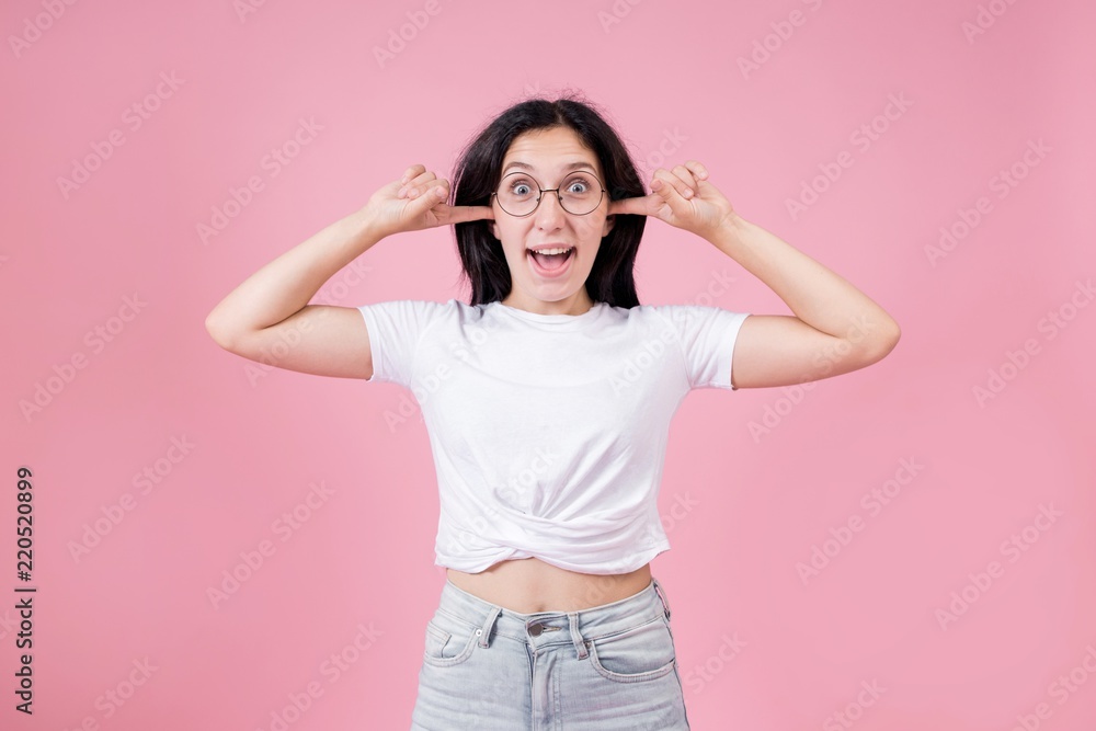 Young beautiful girl in glasses put her hands over her ears standing on pink background Young beautiful girl in glasses put her hands over her ears standing on pink background